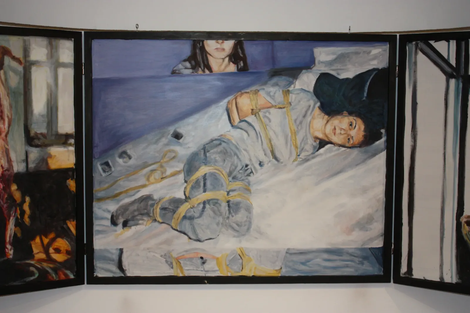 Brussels 3, 2018, vue d'exposition, La montagne, Bruxelles d'Aurian Guerard des Lauriers. Panneau central du triptyque : une personne ligotée de corde jaune est allongée sur un lit, un visage de femme au-dessus.